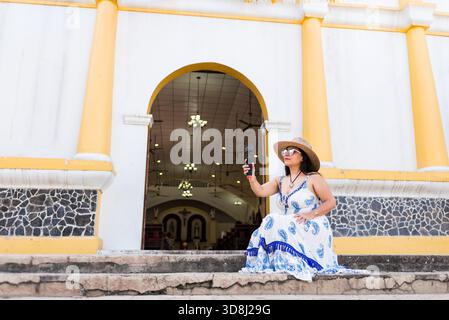 A woman sitting on steps outside a church, holding an action camera. Stock Photo