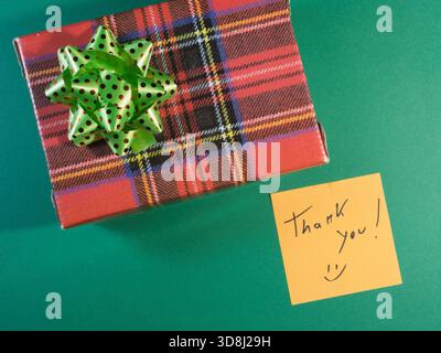 Plaid Gift with Thank You Note - Overhead view of a red plaid gift box with a green polka-dot bow, accompanied by a yellow sticky note expressing grat Stock Photo