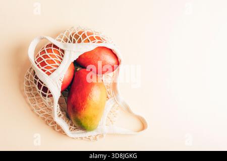 Fresh tropical mango fruits in a cotton mesh bag on a light warm background. Top view, flat lay, copy space. Stock Photo