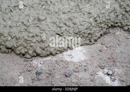 Wet concrete mixture spreading over rough ground surface with stones creating industrial construction background Stock Photo