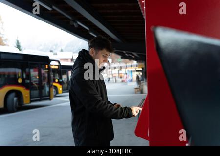 Young man using a ticket vending machine at a bus station in winter Stock Photo