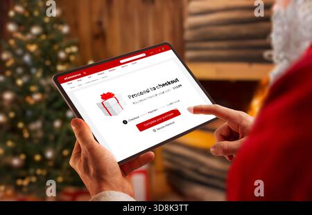 Santa using tablet with holiday checkout screen near fireplace, perfect for ecommerce themes, festive shopping promotions, winter marketing and season Stock Photo