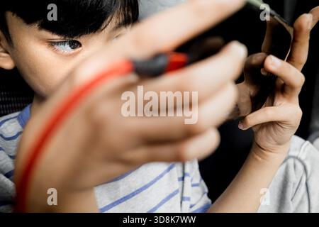 Asian boy playing online game on smartphone while being charged in full concentration inside of a car Stock Photo