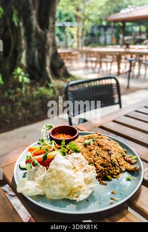 Tasty and famous Indonesian traditional fried rice with chili sauce and fresh vegetables served on table at an outdoor restaurant for lunch Stock Photo