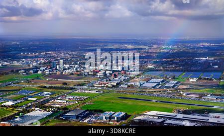 Aerial view of the landscape around Hoofddorp and Schiphol Airport in the Netherlands. A rainbow arches over the green fields, runways, and buildings under a dramatic cloudy sky Stock Photo