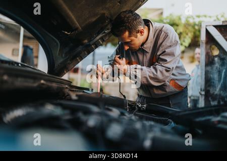 Mechanic inspecting and repairing a car under the hood using a flashlight at a workshop Stock Photo