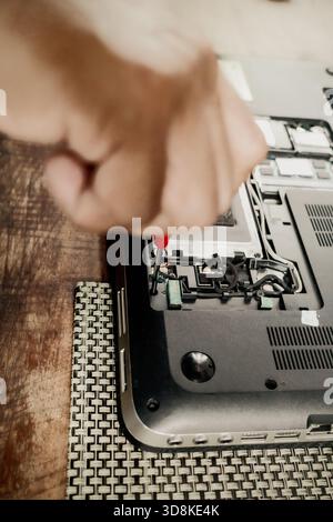 A male person repairing a broken laptop using screwdriver to open up its hardware component parts Stock Photo