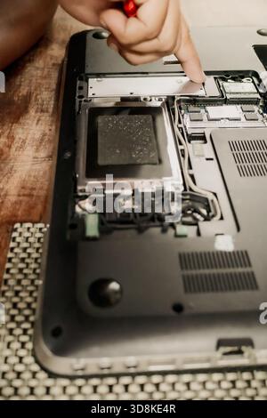 A male person repairing a broken laptop using screwdriver to open up its hardware component parts Stock Photo