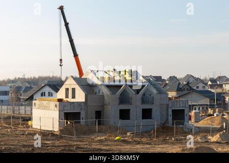 A new concrete two-story house is under construction in a suburban residential development, with a crane visible at the site against a clear sky. Stock Photo