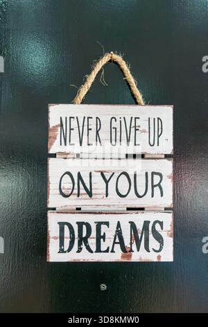 Wooden Sign with Inspirational Text Hanging on Dark Wall Stock Photo
