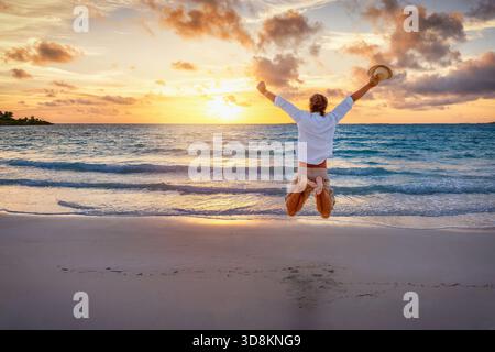 A happy man jumps in the air on a tropical paradise beach during sunrise or sunset time as a concept for success and happiness Stock Photo