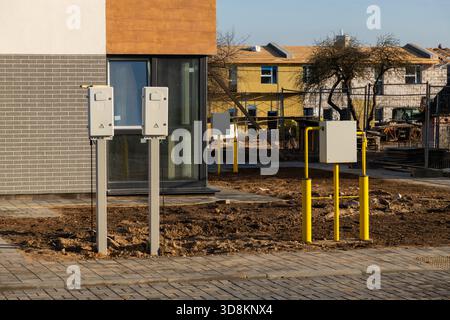 Exterior view of a newly built house with outdoor utility meters and yellow gas pipes installed. A suburban construction site is visible in the backgr Stock Photo