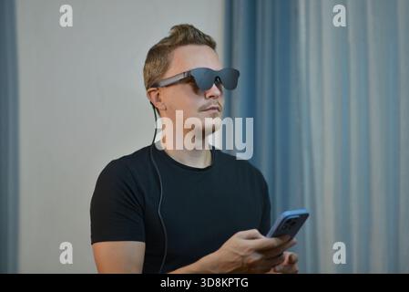 A man wearing modern AR smart glasses connected with smartphone. Futuristic wearable tech, digital eyewear and innovative gadget use in a contemporary Stock Photo