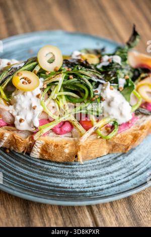 Appetizing lunch. Portion dish. Sandwich with vibrant toppings serving on plate. Food with green grilled leaves beetroot olives yolk sauce. Stock Photo