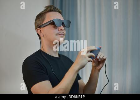 Man wearing modern AR glasses and using a smartphone controller. Futuristic wearable tech, mixed reality device, digital innovation and immersive tech Stock Photo