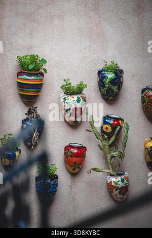 Hand‑painted ceramic planters bring a splash of colour to a stone wall in Mallorca. Overflowing with succulents and greenery. Stock Photo