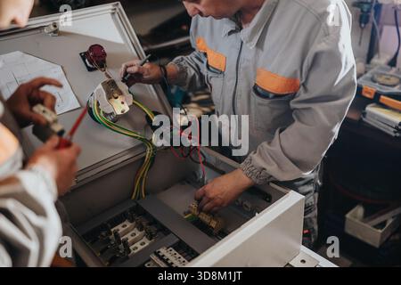 Technicians working on an electrical panel and wiring in a workshop, assembling and testing components Stock Photo