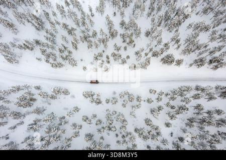 Aerial view over car / van driving over snow covered road through the taiga in winter, Riisitunturi National Park, Lapland, Posio, Koillismaa, Finland Stock Photo