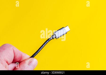 USB-C cable held in hand against a bright yellow background Stock Photo