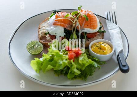 Toast with poached eggs, tomato and salmon on plate in cafe, close up, breakfast time Stock Photo