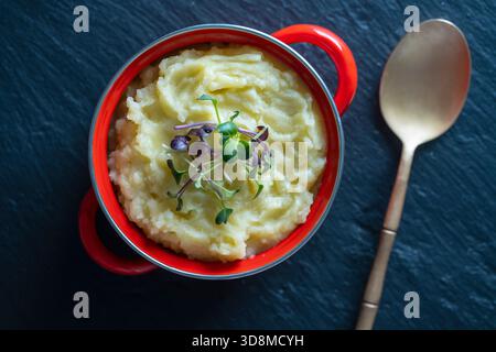 Mashed potatoes with radish microgreens in a red saucepan close up, top view Stock Photo