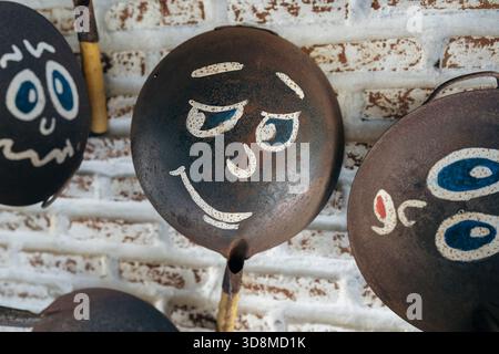 Old frying pans with painted faces, hang on a brick wall, close up Stock Photo