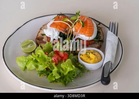 Toast with poached eggs, tomato and salmon on plate in cafe, close up, breakfast time Stock Photo