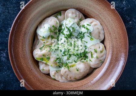 Appetizing dumplings stuffed with potatoes and mushrooms with sour cream and green dill on a ceramic plate, close up, top view. Homemade Ukrainian cui Stock Photo