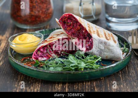 Vegan burrito. Sliced up raw food wrap with red beetroot, feta cheese, prunes, dill and cream sauce with pea microgreens on a plate. Close up Stock Photo