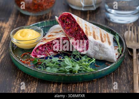 Vegan burrito. Sliced up raw food wrap with red beetroot, feta cheese, prunes, dill and cream sauce with pea microgreens on a plate. Close up Stock Photo