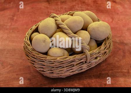 Freshly harvested potatoes in an old wicker basket on a wooden table Stock Photo