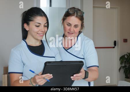 Two female healthcare workers reviewing information together on a black board, smiling and discussing their work in a clinical setting. Stock Photo