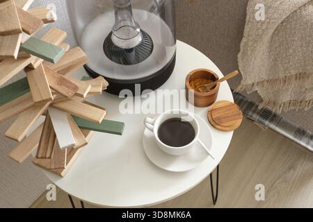 Coffee cup and home speaker resting on a white side table next to a cozy couch Stock Photo