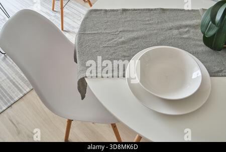 Modern table set with a cloth runner, plates, bowl, and a scandinavian style chair Stock Photo