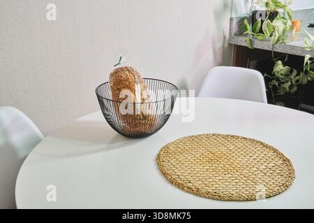Whole grain bread in a wire basket on a white table with a placemat Stock Photo