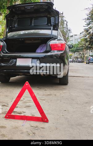 Black car with open trunk showing a red warning triangle on the pavement Stock Photo