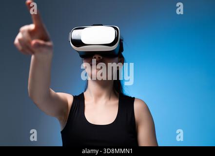 Woman interacting with virtual interface using VR headset and extended hand in clean futuristic blue studio Stock Photo