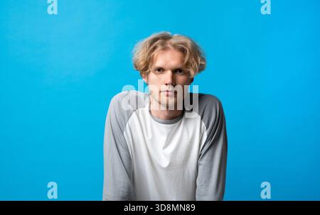 Thoughtful young man leaning slightly forward with serious expression on bright blue background Stock Photo