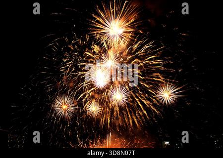 Vibrant orange-yellow fireworks burst in spectacular patterns against the night sky, symbolizing celebration and collective joy. Stock Photo