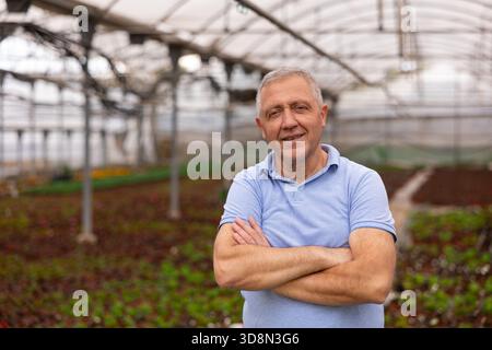 Old man worker posing joyfully in greenhouse Stock Photo