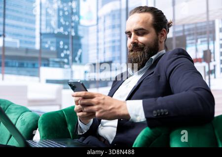 Determined chief executive officer analyzing stock market trends, browsing the web on his smartphone and ensuring company efficiency. Builds a growing business empire at the office. Stock Photo