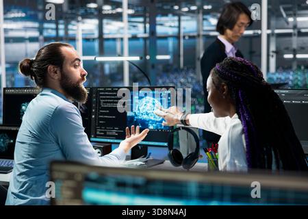 Teamworking programmers in data center troubleshoot server connectivity issues using AI. Colleagues working together in server room auditing systems for vulnerabilities using artificial intelligence Stock Photo