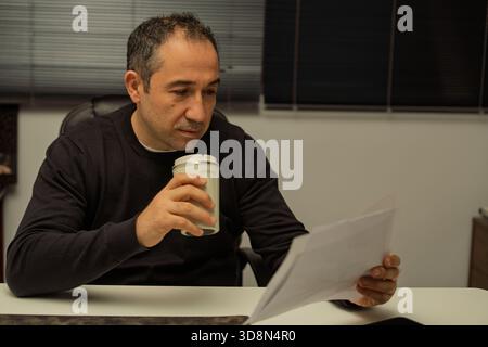 Businessman concentrating on reading financial documents while holding a reusable coffee cup in an office Stock Photo