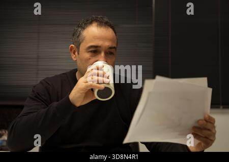 Man focused, reviewing paperwork and drinking from a travel mug Stock Photo