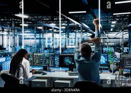 Data center computer scientist relaxing joints to combat sedentary fatigue after working long hours at desk. Server hub software developer feeling pain from incorrect posture at workstation Stock Photo