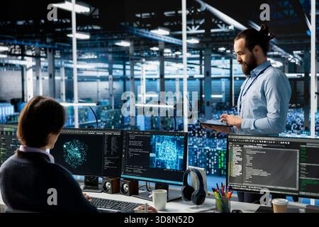 System administrators monitoring AI LLM visualization in data center with server racks rows. IT specialists oversee mainframes powering deep learning in server hub built for digital storage systems Stock Photo