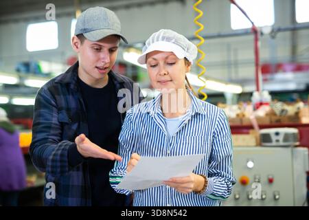 Workers of fruit storage and sorting facility talking about work process standing near the conveyor line and tangerine boxes. Stock Photo
