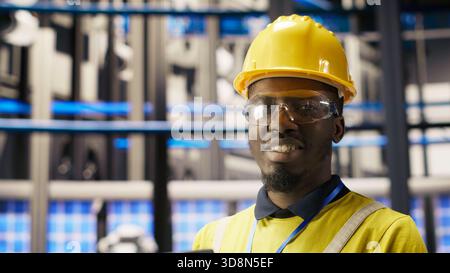 Professional working in smart factory, testing automated systems to ensure reliability. African american man in industry 4.0 plant using notebook to identify bottlenecks and optimize, camera B Stock Photo