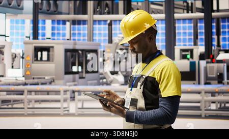 Technician in industrial plant using tablet app to diagnose equipment errors. Manufacturing factory specialist using digital device to coordinate repair tasks on assembly lines, camera A Stock Photo