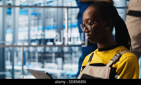 Worker using tablet in smart factory, collecting and analyzing data. Expert using tracking software on device in industry 4.0 industrial plant equipped with advanced sensors, camera A close up Stock Photo